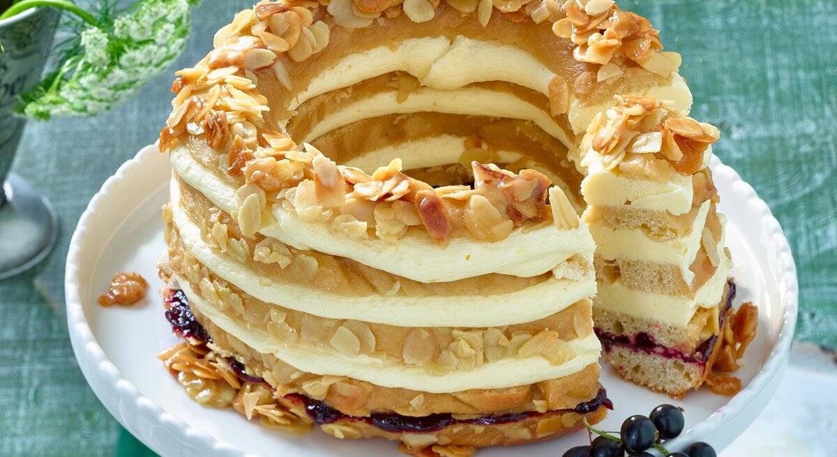 Der Johannisbeer-Bienenstichkranz auf einer weißen Etagere mit dunkelgrünem Untergrund. Alles von schräg oben fotografiert.