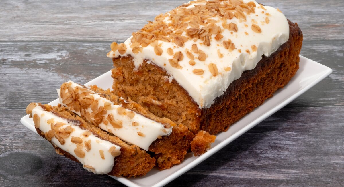 Karottenkuchen mit Creme drapiert auf weißer Platte auf grauem Holz.