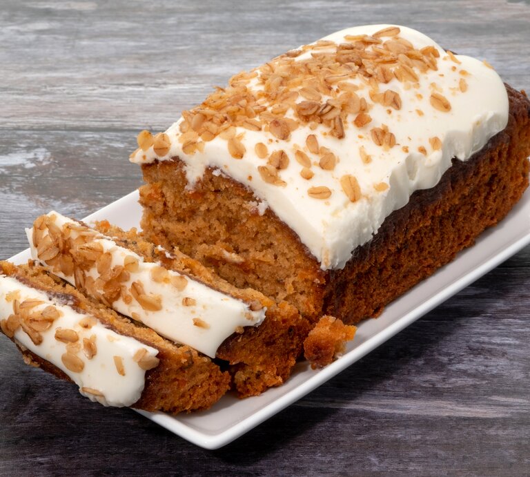Karottenkuchen mit Creme drapiert auf weißer Platte auf grauem Holz. | © Getty Images/clubfoto