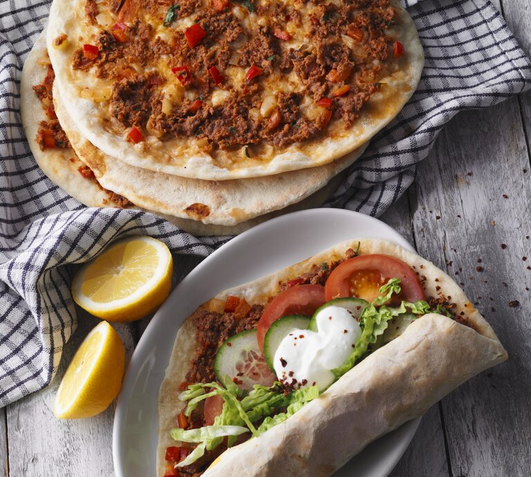 Draufsicht: Vier türkische Pizza Lahmacun. Drei nur mit Hackfleisch, eine mit Tomaten, Gurkenscheiben, Salat und Joghurtsauce | © StockFood / Gräfe & Unzer Verlag / Kramp + Gölling