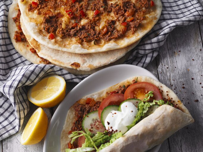 Draufsicht: Vier türkische Pizza Lahmacun. Drei nur mit Hackfleisch, eine mit Tomaten, Gurkenscheiben, Salat und Joghurtsauce | © StockFood / Gräfe & Unzer Verlag / Kramp + Gölling