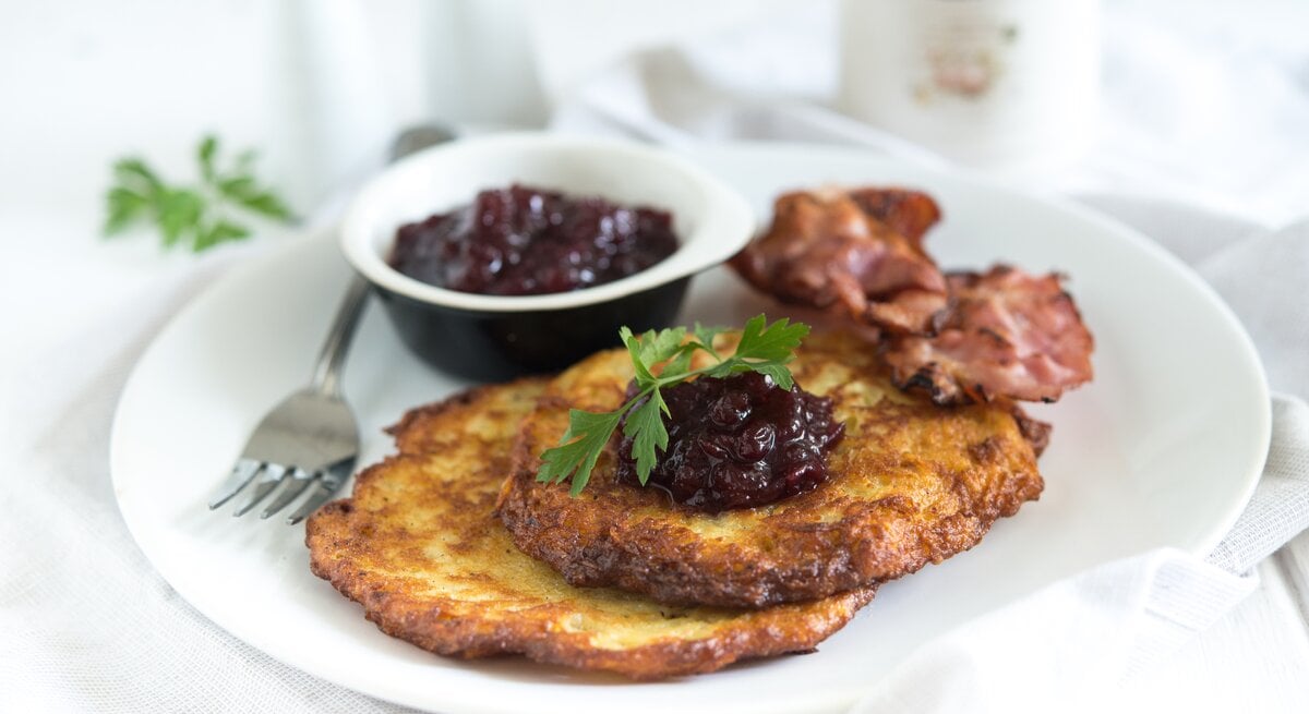 Zwei schwedische Kartoffelpfannkuchen mit Speck und Preiselbeeren auf hellem Teller. 