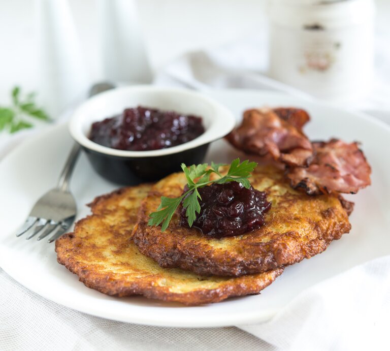 Zwei schwedische Kartoffelpfannkuchen mit Speck und Preiselbeeren auf hellem Teller.  | © iStock/PingPongCat