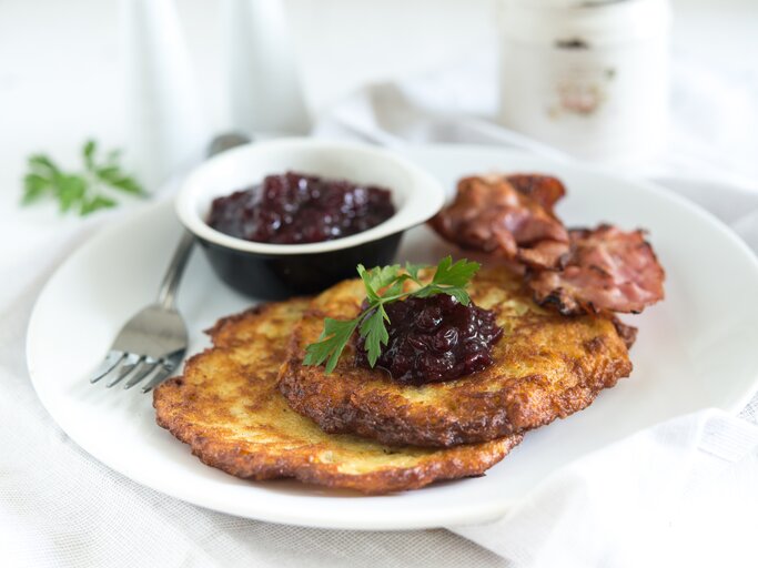 Zwei schwedische Kartoffelpfannkuchen mit Speck und Preiselbeeren auf hellem Teller.  | © iStock/PingPongCat