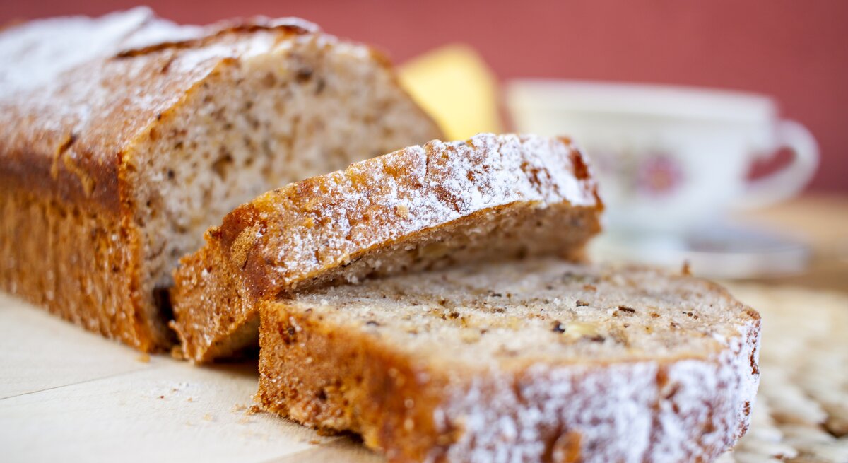 Bananen-Kastenkuchen mit Schokoflakes und mit Puderzucker bestreut auf Holzbrett. 