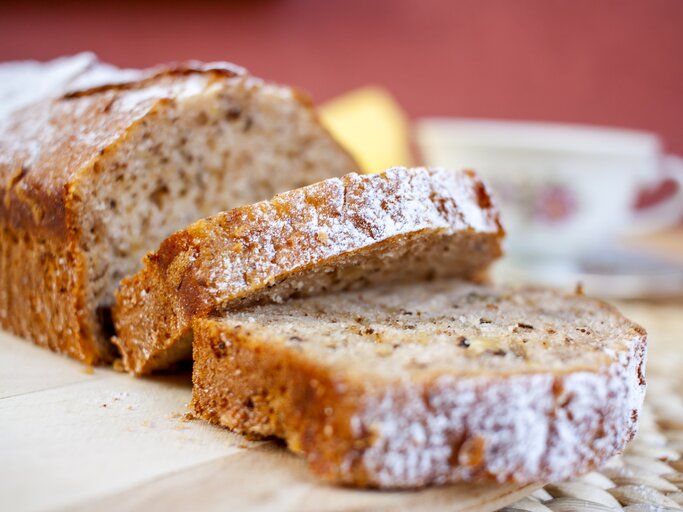 Bananen-Kastenkuchen mit Schokoflakes und mit Puderzucker bestreut auf Holzbrett.  | © iStock/ SonjaBK