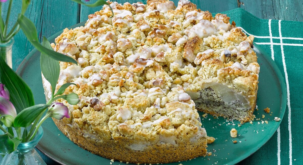 Der Mohnkuchen auf einem türkisenen Teller und türkisen Holztisch. Alles von der Seite fotografiert.