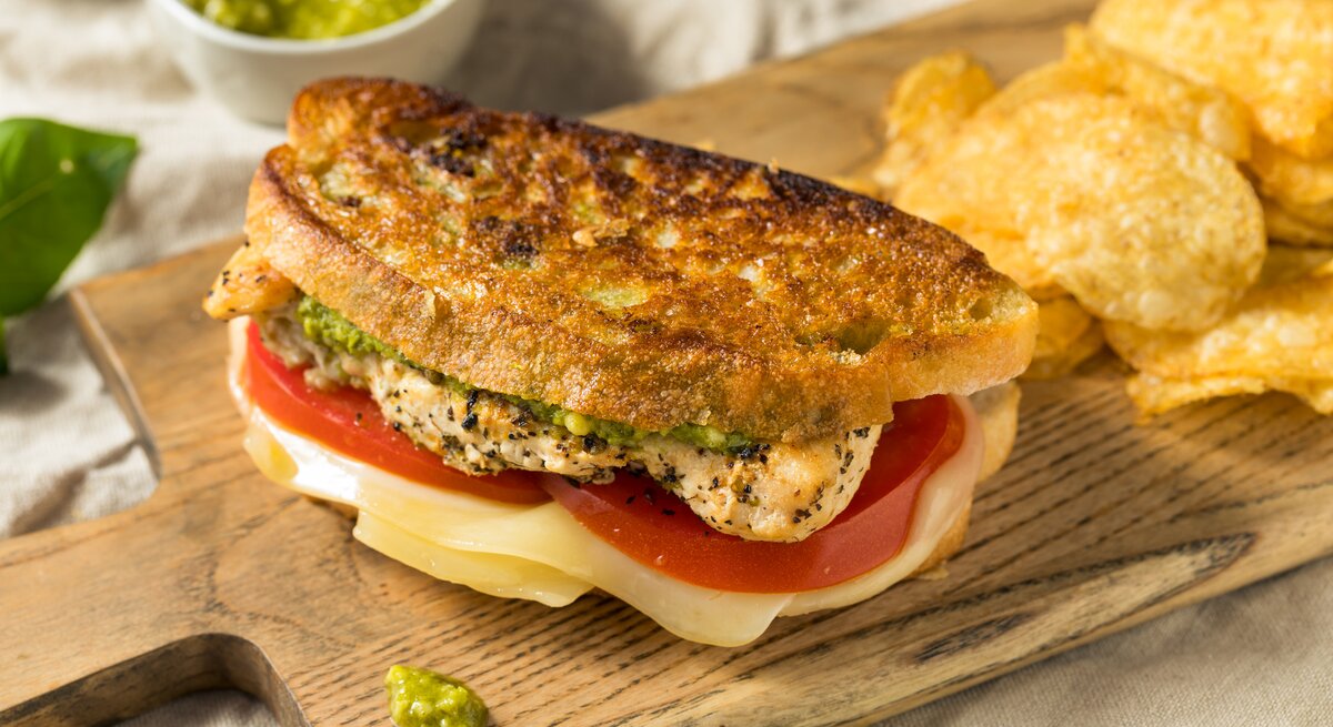 Belegtes Chicken-Sandwich auf Holzbrett mit Chips als Deko.