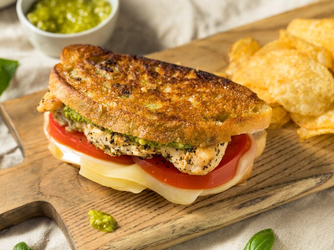 Belegtes Chicken-Sandwich auf Holzbrett mit Chips als Deko. | © iStock.com/bhofack2