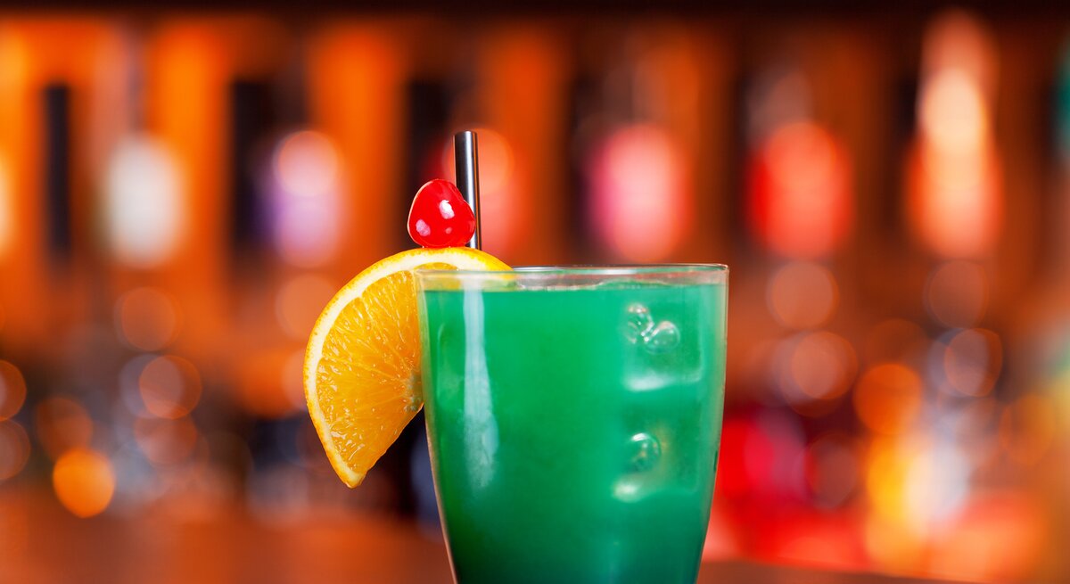 Leuchtend-grüner Cocktail in einem kleinen Trinkglas, dekoriert mit einer Orangenscheibe und einer Cocktailkirsche, 
