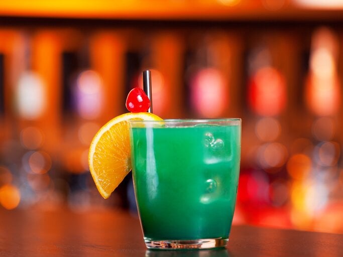 Leuchtend-grüner Cocktail in einem kleinen Trinkglas, dekoriert mit einer Orangenscheibe und einer Cocktailkirsche,  | © iStock/ivanmateev