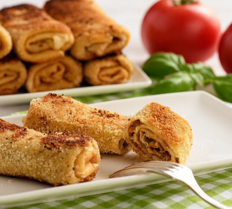 Panierte gerollte Pfannkuchen auf rechteckigem Teller.  | © iStock/iko636