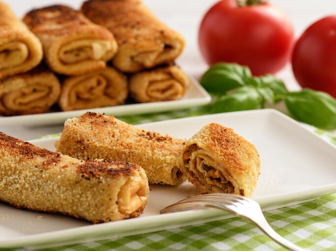 Panierte gerollte Pfannkuchen auf rechteckigem Teller.  | © iStock/iko636