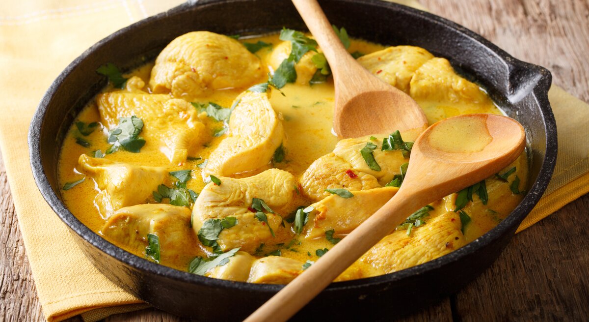 Gusseiserne Pfanne mit Hähnchen-Curry auf hölzernem Untergrund. 
