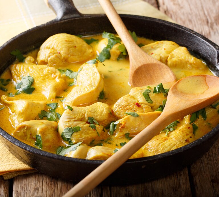 Gusseiserne Pfanne mit Hähnchen-Curry auf hölzernem Untergrund.  | © GettyImages/ALLEKO