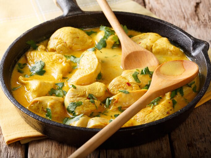 Gusseiserne Pfanne mit Hähnchen-Curry auf hölzernem Untergrund.  | © GettyImages/ALLEKO