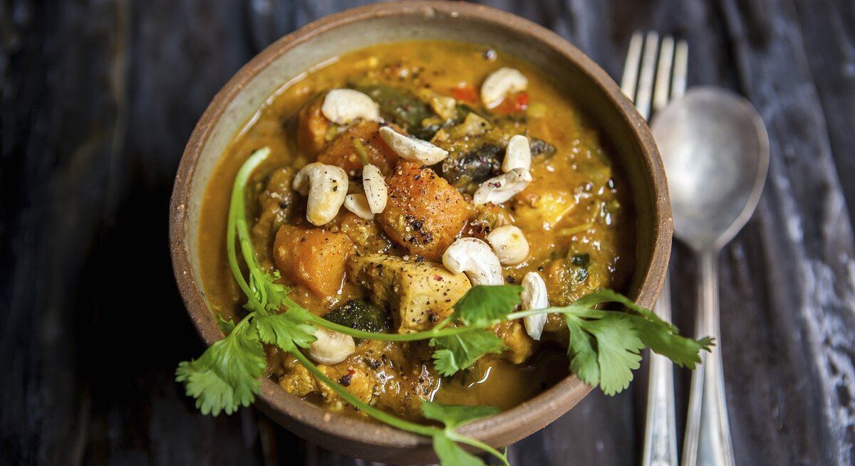 Cremiges Süßkartoffel-Curry mit Hähnchen und Cashews, garniert mit frischem Koriander in einer Schale auf dunklem Holztisch.