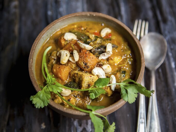 Cremiges Süßkartoffel-Curry mit Hähnchen und Cashews, garniert mit frischem Koriander in einer Schale auf dunklem Holztisch. | © StockFood/Thorpe, Lara Jane