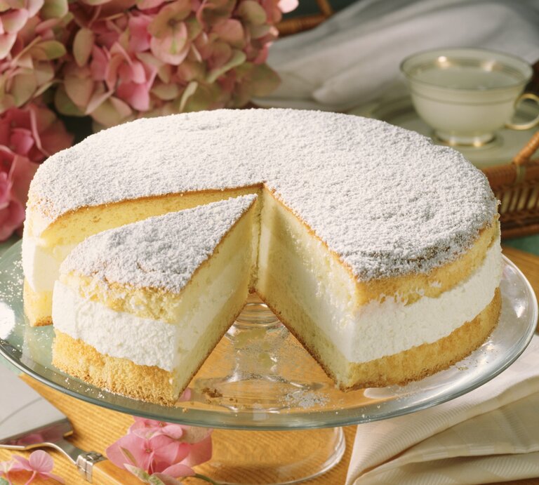 Die Käse-Sahne-Torte auf einem grünlichen Tisch mit pinken Blüten im Hintergrund. | © StockFood