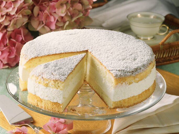 Die Käse-Sahne-Torte auf einem grünlichen Tisch mit pinken Blüten im Hintergrund. | © StockFood