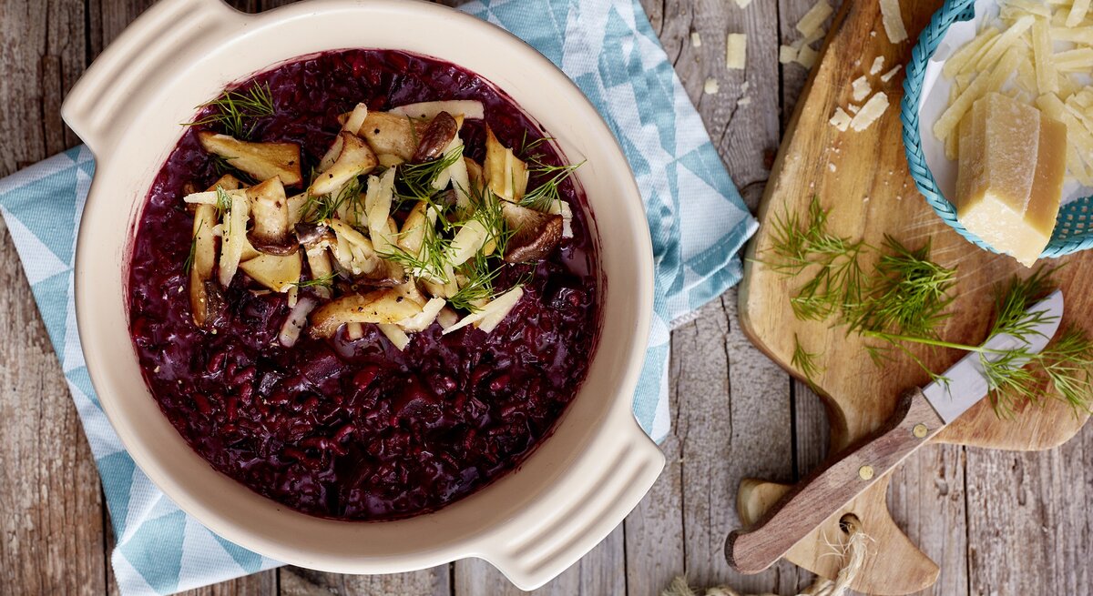 Rote Bete Risotto auf hölzernem Hintergrund. Rechts davon Parmesan.