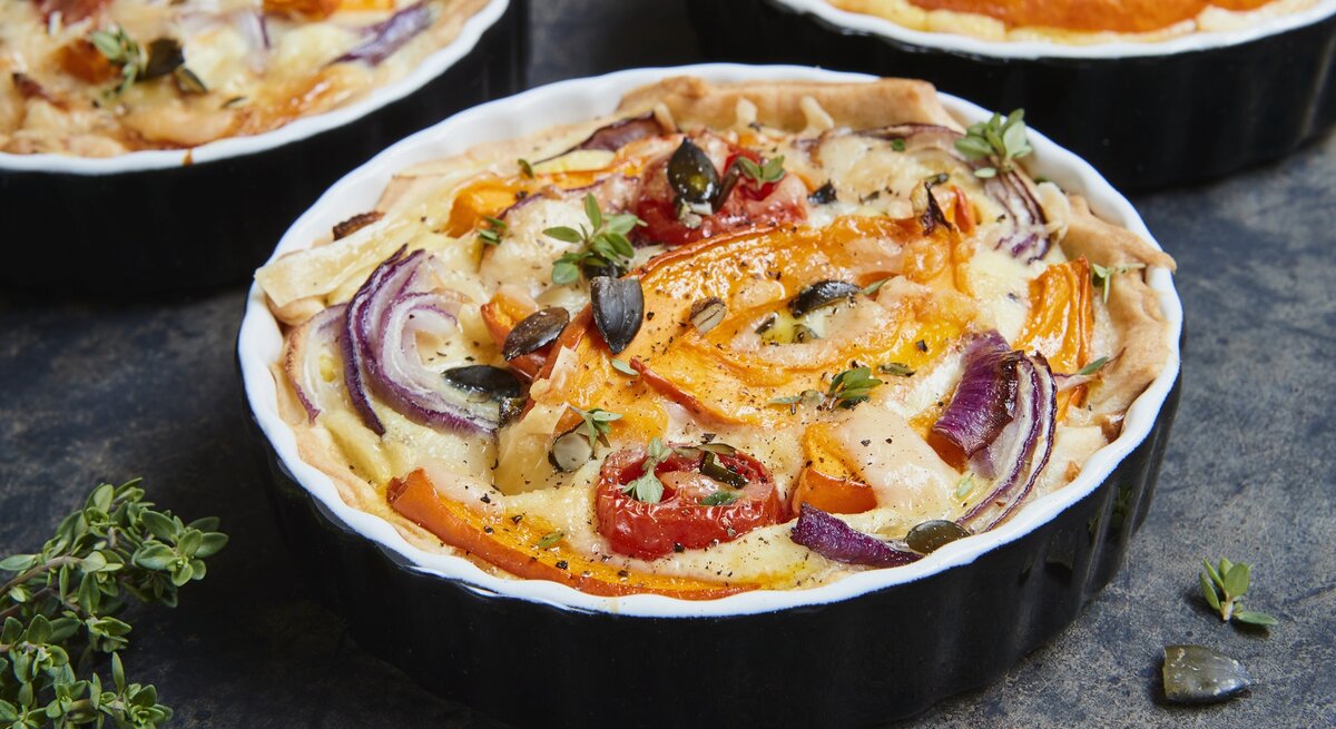 Die Kürbis-Quiche mit roten Zwiebeln in einer schwarzen Auflaufform gebacken.