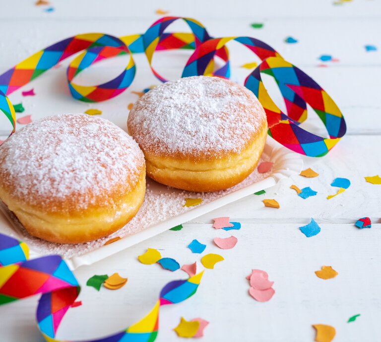zwei Berliner mit Puderzucker bestäubt in weißem Szenario. Daneben Konfetti und Luftschlangen. | © iStockphoto.com/Sonja Rachbauer 