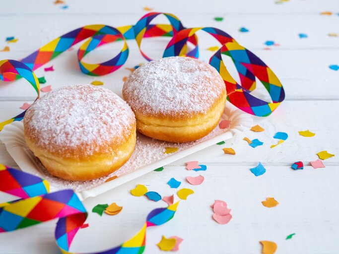 zwei Berliner mit Puderzucker bestäubt in weißem Szenario. Daneben Konfetti und Luftschlangen. | © iStockphoto.com/Sonja Rachbauer 