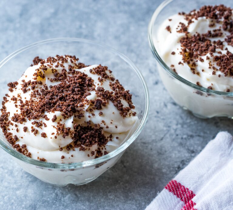 Weiße Quark-Bananen-Creme mit Kekskrümeön auf himmelblauer Oberfläche. | © iStock.com/alpaksoy