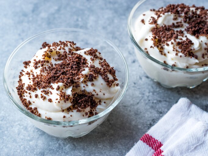 Weiße Quark-Bananen-Creme mit Kekskrümeön auf himmelblauer Oberfläche. | © iStock.com/alpaksoy
