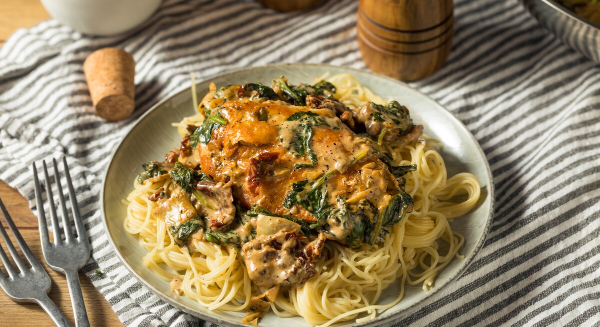 Toskanische Hähnchenpfanne mit Spaghetti, Spinat und getrockneten Tomaten auf weißem Teller. 