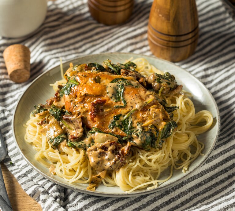Toskanische Hähnchenpfanne mit Spaghetti, Spinat und getrockneten Tomaten auf weißem Teller.  | © iStock.com/bhofack2