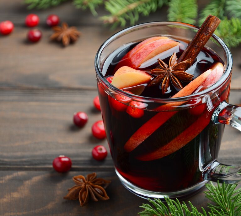 Eine durchsichtige Tasse gefüllt mit selbst gemachtem Glühwein auf Holztisch. Daneben weihnachtliche Gewürze und Deko-Elemente.  | © iStock/ JulijaDmitrijeva