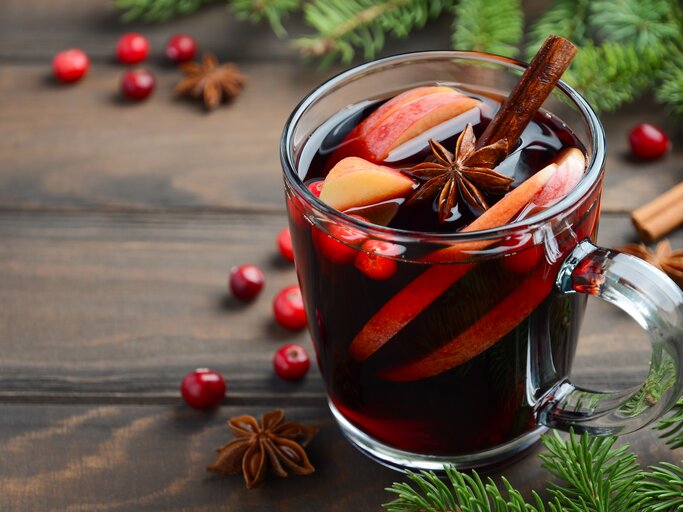 Eine durchsichtige Tasse gefüllt mit selbst gemachtem Glühwein auf Holztisch. Daneben weihnachtliche Gewürze und Deko-Elemente.  | © iStock/ JulijaDmitrijeva