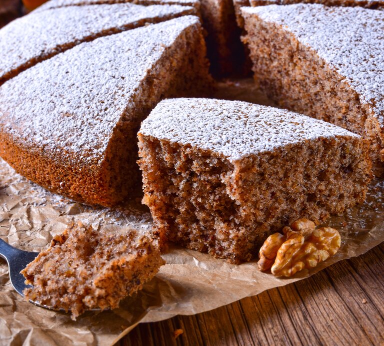 Ein angeschnittener Walnusskuchen mit Schokolade, bestäubt mit Puderzucker, auf einem Holztisch mit Backpapier.  | © iStock.com/Dar1930