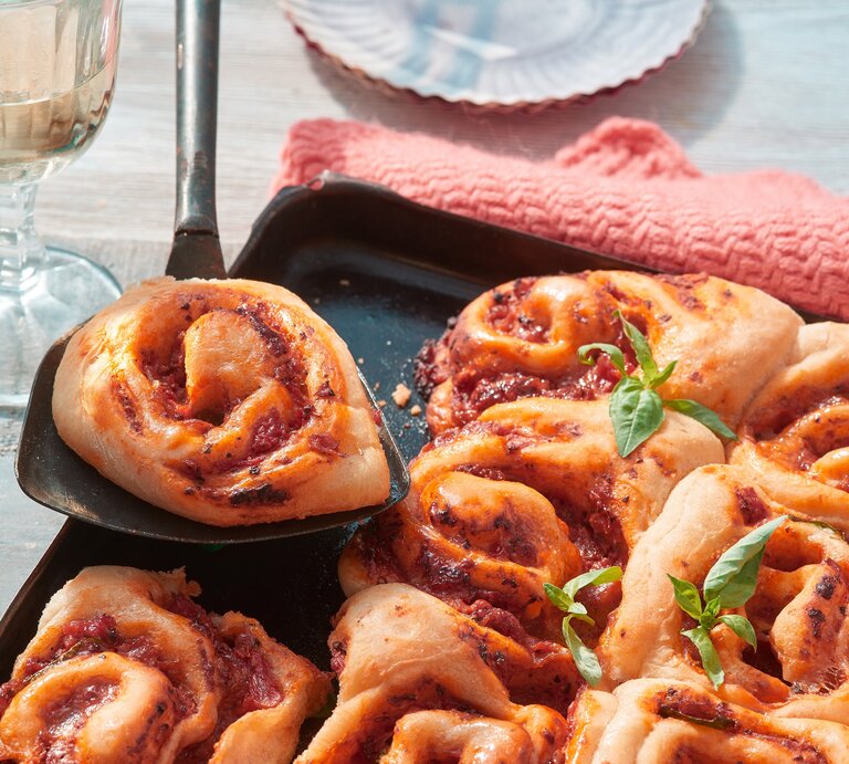 Pizza-Schnecken vom Blech auf einem schwarzen Blech auf hölzernem Hintergrund. Links ein Glas Sekt. | © Matthias Liebich