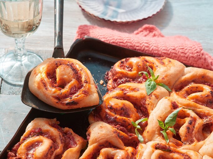 Pizza-Schnecken vom Blech auf einem schwarzen Blech auf hölzernem Hintergrund. Links ein Glas Sekt. | © Matthias Liebich