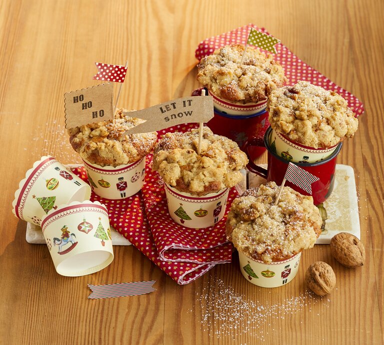 Bratapfel-Walnuss-Muffins auf einem hellen Holztisch mit roter Tischdecke. Alles von schräg oben fotografiert. | © StockFood / Winner, Katrin