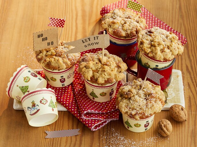 Bratapfel-Walnuss-Muffins auf einem hellen Holztisch mit roter Tischdecke. Alles von schräg oben fotografiert. | © StockFood / Winner, Katrin