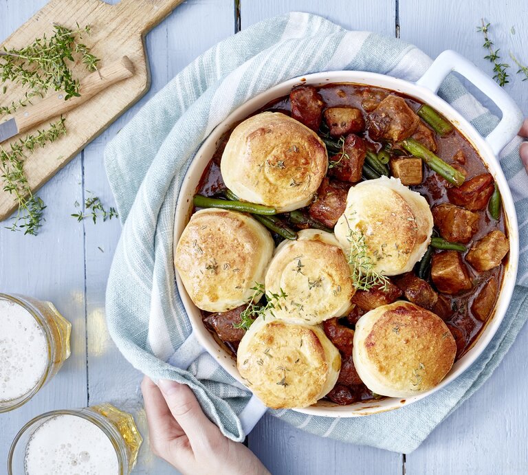 Bier-Gulasch mit Brötchen in einem weißen Topf auf hellem Hintergrund. | © EAT CLUB/Isabell Triemer