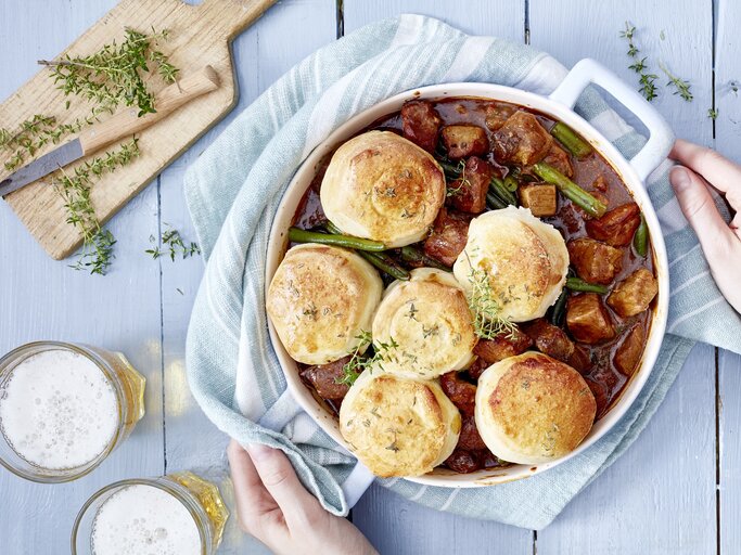 Bier-Gulasch mit Brötchen in einem weißen Topf auf hellem Hintergrund. | © EAT CLUB/Isabell Triemer