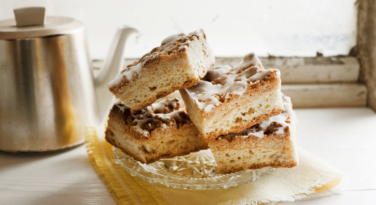 Mehrere Kuchenstücke auf einem hellen Kaffeetisch mit Kanne im Hintergrund.