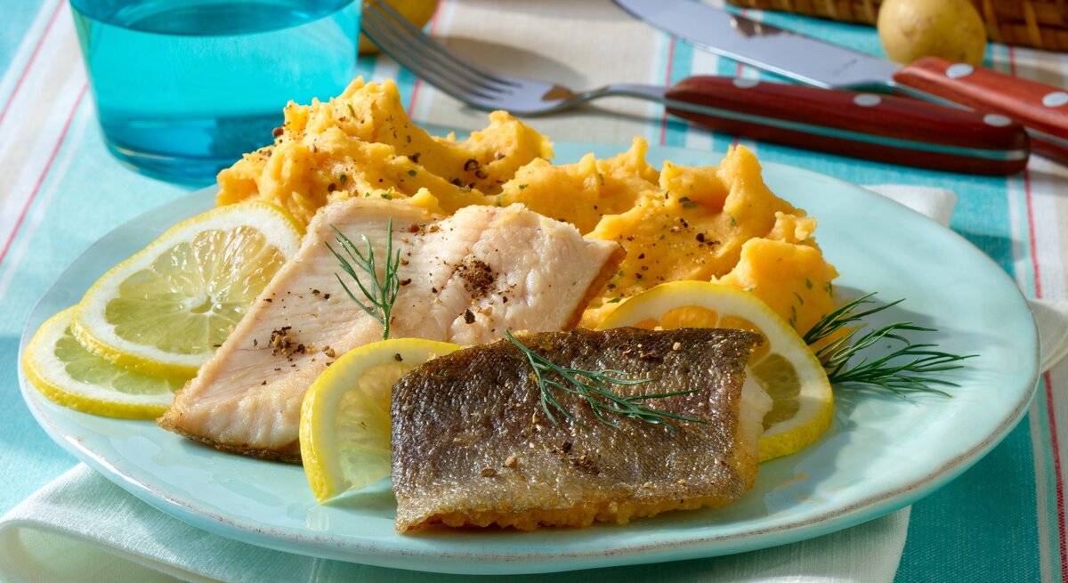 Ein Teller Kartoffel-Kürbis-Püree zu Forellenfilet auf einem Tisch / Besteck / Glas / Tuck / rohe Kartoffeln im Korb