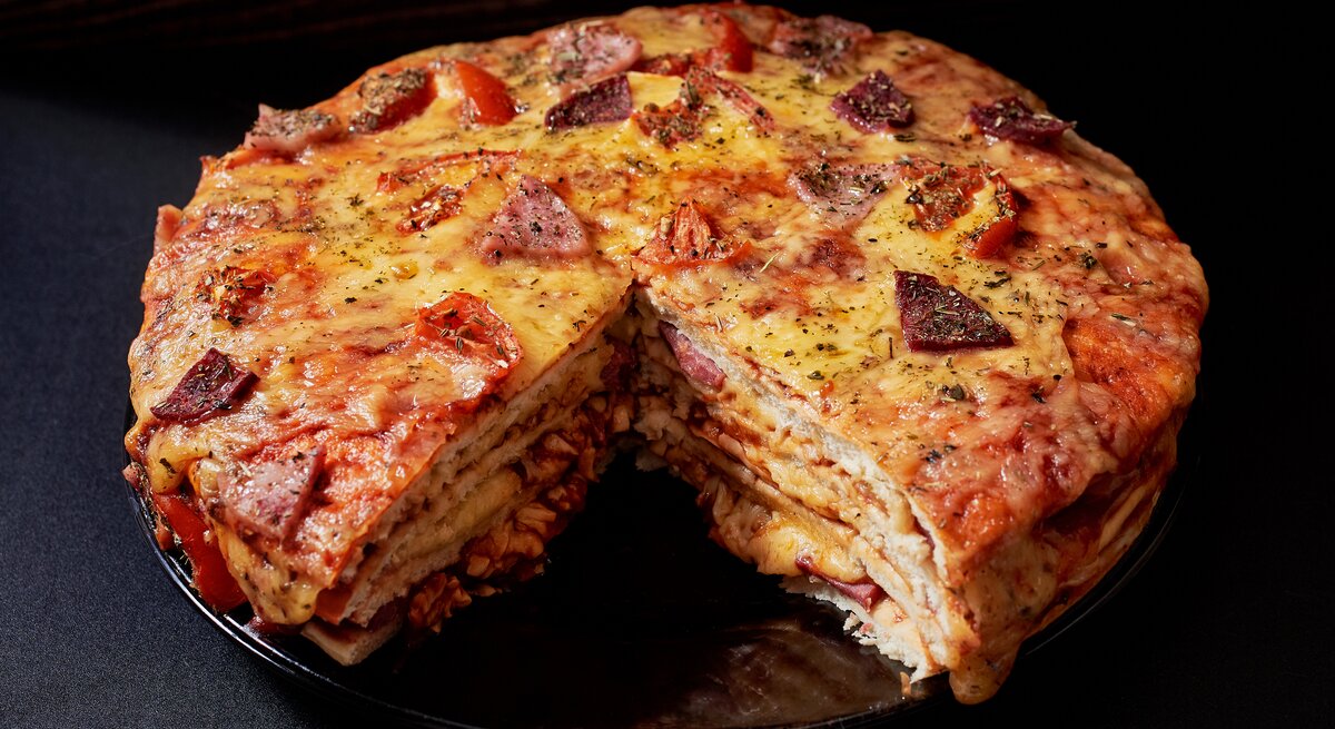 Gestapelter Pizzakuchen mit Käse, Schinken und Salami in dunkler Kulisse. 