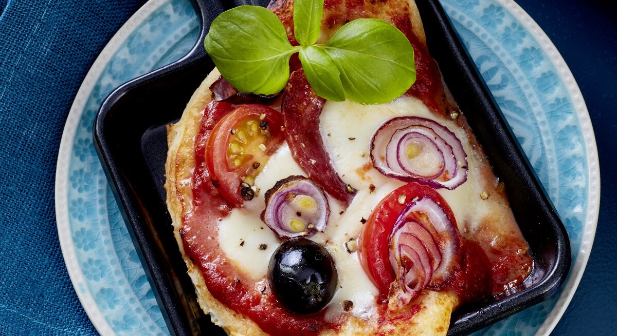 Salami-Pizza-Pfännchen auf einem blauen Teller auf blauem Hintergrund. 
