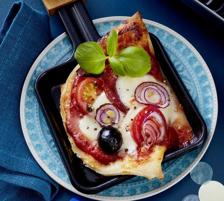 Salami-Pizza-Pfännchen auf einem blauen Teller auf blauem Hintergrund.  | © EAT CLUB / Isabell Triemer
