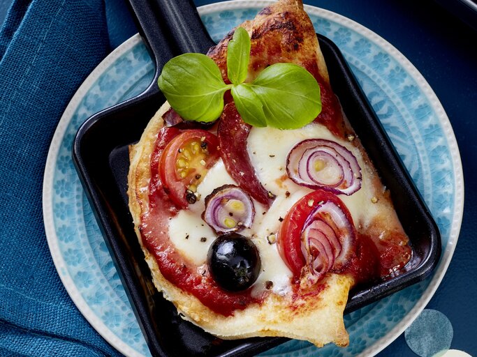 Salami-Pizza-Pfännchen auf einem blauen Teller auf blauem Hintergrund.  | © EAT CLUB / Isabell Triemer