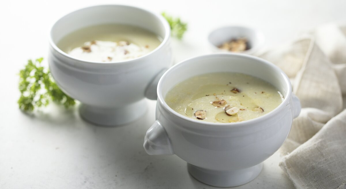 Weiße Suppenschalen gefüllt mit Kohlrabicremesuppe, garniert mit Haselnuss. 