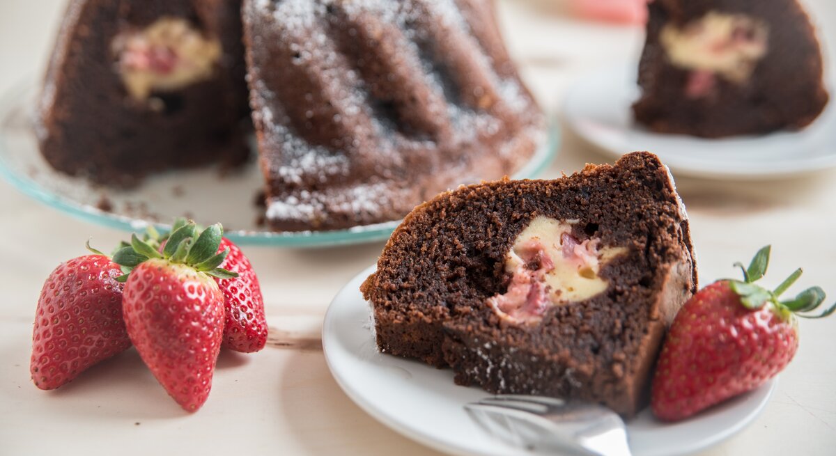 Mit Käsekuchen gefüllter Schokokuchen mit Erdbeeren auf weißem Teller. 