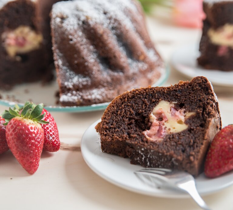 Mit Käsekuchen gefüllter Schokokuchen mit Erdbeeren auf weißem Teller.  | © Getty Images/A_Lein
